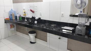 A kitchen with a black countertop, white cabinets, a gas stove, a blender, and a fan.