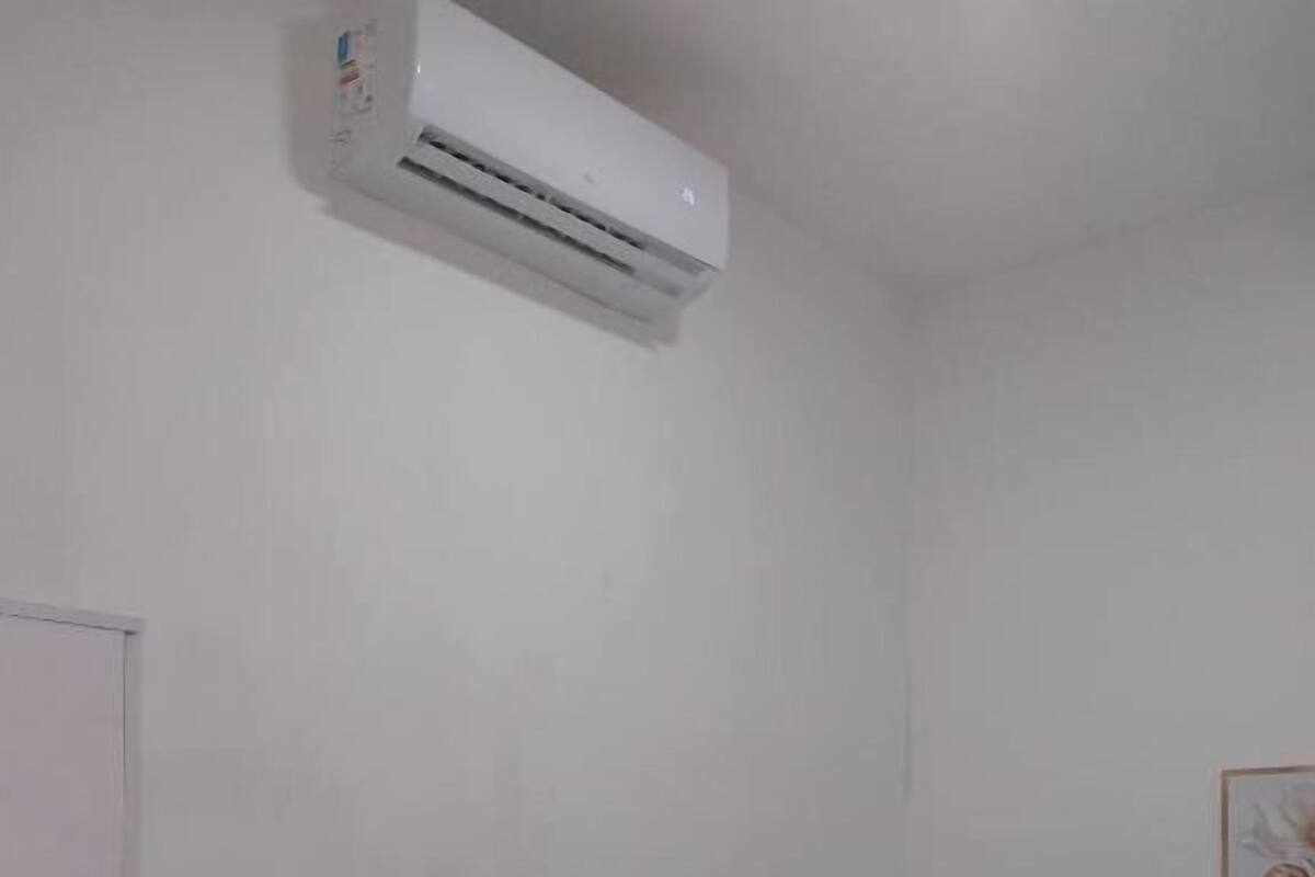 Una habitación pequeña con una cama, una silla y un equipo de aire acondicionado en la pared.
