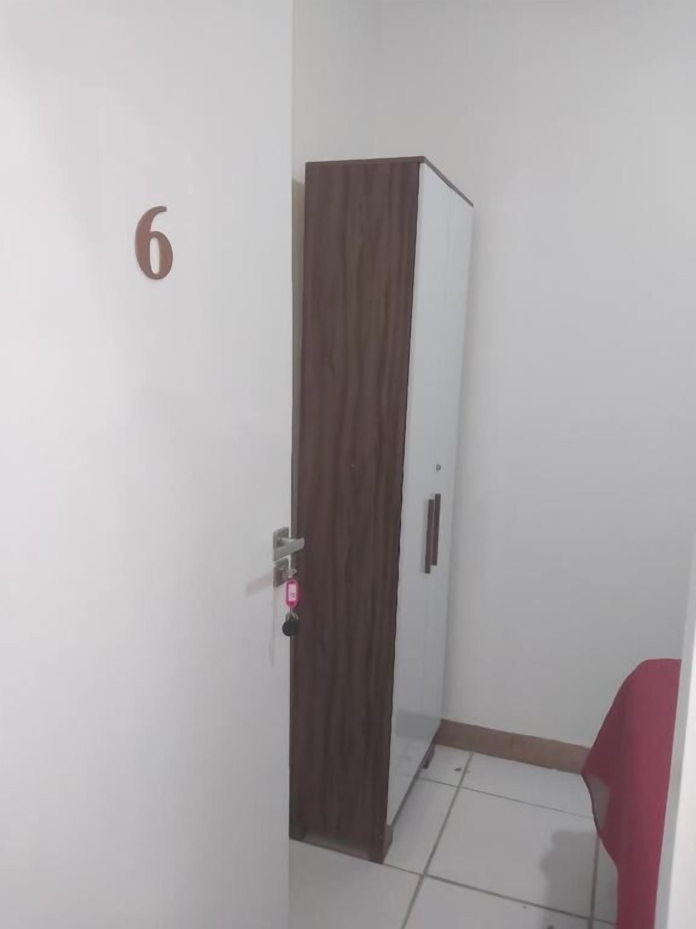 Een kamer met een kledingkast, een deur met het cijfer '6' erop en een rode stoel.