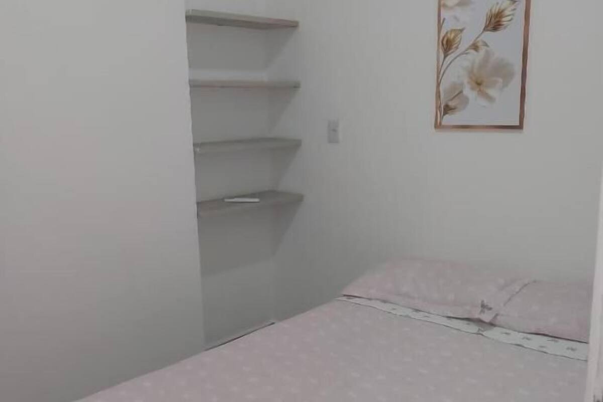 Un dormitorio pequeño y ordenado con una cama individual, una estantería en la pared y una obra de arte floral enmarco.