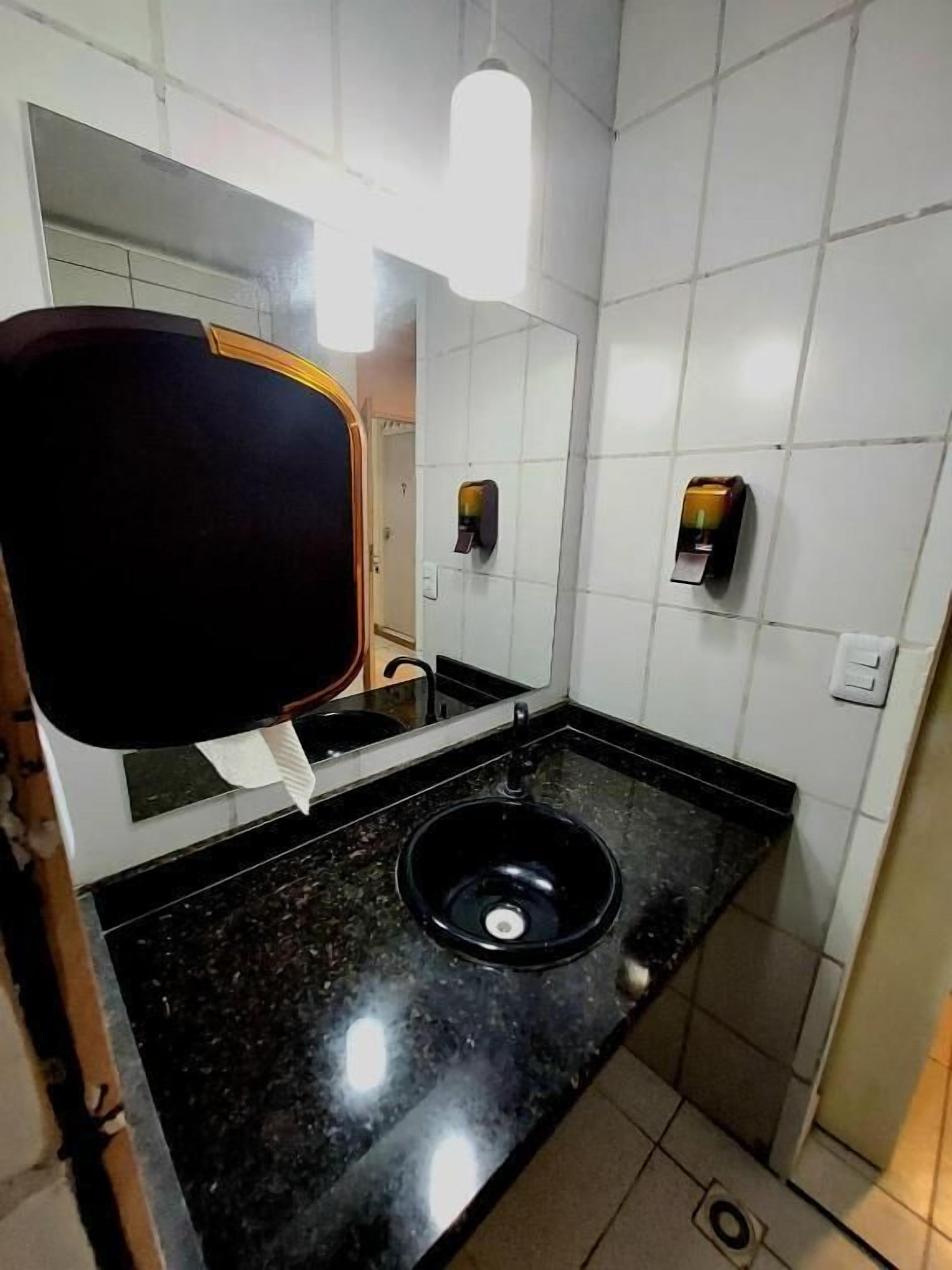 Casa de banho com lavatório preto, espelho e secador de mãos.