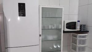 Una cocina con un refrigerador blanco, un microondas y un armario con puerta de vidrio y estantes.