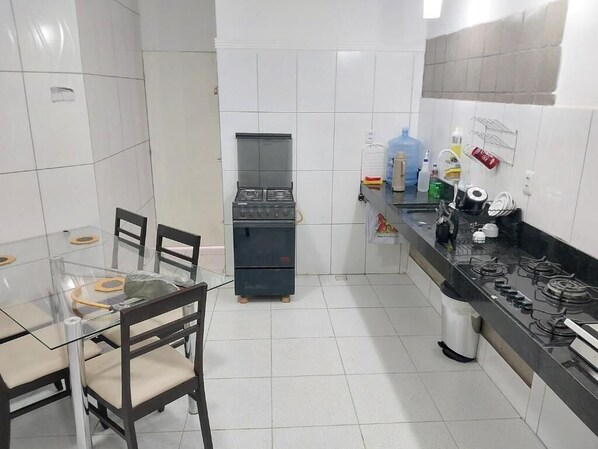 A kitchen with a gas stove, a refrigerator, and a dining area with a glass table and chairs. - Fenix Hospedaria (Natal)