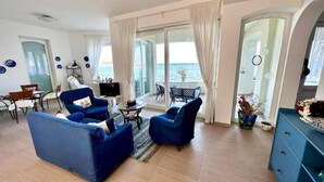 A living room with a sofa, armchairs, a TV, and a balcony with a view of the sea. - Casa Alba Serena by the sea (Marzamemi)