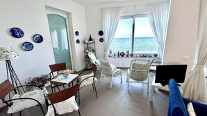 A room with a dining table, chairs, a TV, and a view of the sea. - Casa Alba Serena by the sea (Marzamemi)