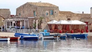 A waterfront area with boats docked, a building with outdoor seating, and a clear sky. - Casa Alba Serena by the sea (Marzamemi)