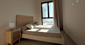 Ein Schlafzimmer mit einem Bett, einem Nachttisch, einer Lampe und einem Fenster mit Vorhängen.