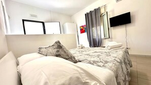 Una habitación de hotel con una cama, un televisor de pantalla plana montado en la pared, una ventana con cortinas y un perchero para toallas.