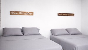 Two beds with grey bedding and pillows, a wooden sign with 'Vive Rio Ama' on the left, and another sign with 'La vida es mejor con amigos' on the right. - Modern Apartment w Private Pool (Chiquimulilla)