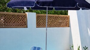 A poolside area with a round glass table and four striped chairs, a dark blue umbrella, and wooden lattice panels. - Modern Apartment w Private Pool (Chiquimulilla)