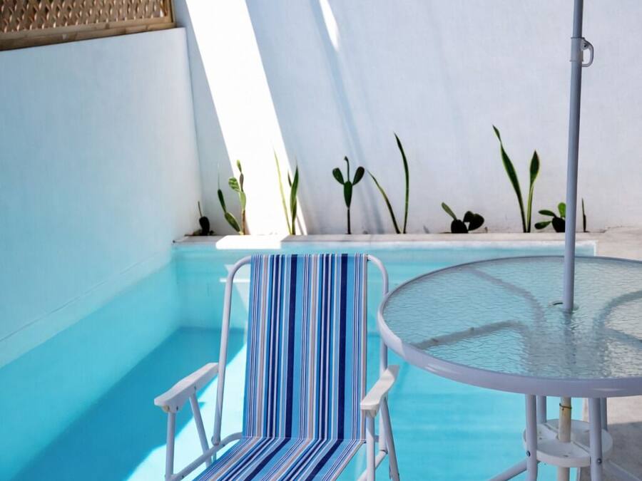 Un área junto a la piscina con una silla de reposo, una mesa y una sombrilla.