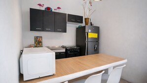 A compact kitchen with a white microwave, a stove, and a refrigerator. There are black cabinets above the counter and a small vase with dried flowers on the refrigerator. - Modern Apartment with Private Pool (Chiquimulilla)