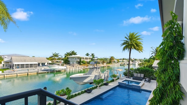 A swimming pool with lounge chairs and a boat dock, surrounded by palm trees and a clear sky.