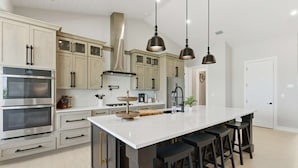 A modern kitchen with stainless steel appliances, a large island with bar stools, and pendant lighting.
