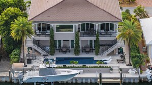 A two-story house with a swimming pool, a boat docked at the front, and a well-maintained garden.