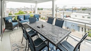 A covered balcony with a table and chairs, a sofa with blue cushions, and a view of the cityscape. - Spacious, 5 Bedroom/3.5 Bath In The Hear of Ocean City (Ocean City)