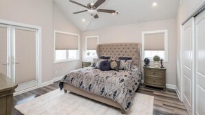 A bedroom with a tufted headboard, a large bed, a ceiling fan, and a window with blinds. - Spacious, 5 Bedroom/3.5 Bath In The Hear of Ocean City (Ocean City)