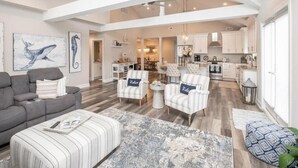 A spacious living area with a gray sofa, striped ottoman, and two armchairs with pillows. A dining area is visible in the background with a kitchen. - Spacious, 5 Bedroom/3.5 Bath In The Hear of Ocean City (Ocean City)