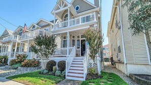 A two-story house with a front porch, a small front yard, and a flag. - Spectacular Southend 3BR Condo • Sleeps 7 • Rooftop Deck & Parking (Ocean City)