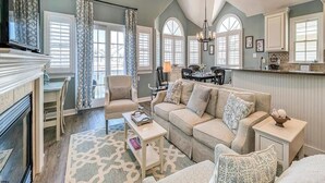 A spacious living room with a fireplace, a sofa, a coffee table, and a dining area with a table and chairs. - Spectacular Southend 3BR Condo • Sleeps 7 • Rooftop Deck & Parking (Ocean City)