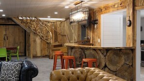 Un intérieur rustique avec un escalier en bois, un coin bar avec des tabourets et un canapé en cuir.