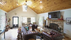 Un salon spacieux doté d’un haut plafond en bois, d’une cheminée et d’un téléviseur.