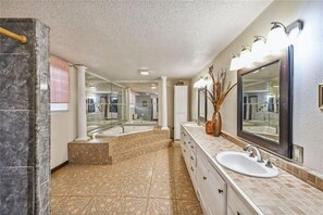 Une salle de bain spacieuse avec un grand miroir, deux lavabos, une baignoire et un meuble-lavabo avec des tiroirs.