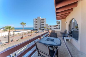 Un balcon avec une table et des chaises, donnant sur une plage et des immeubles.