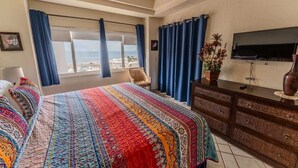 A hotel room with a bed, a television, a dresser, and a view of the beach. - Delphin 504 Las Palmas Resort (Puerto Peñasco)