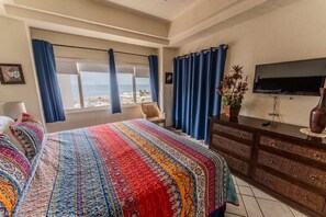 A hotel room with a bed, a television, a dresser, and a view of the beach. - Delphin 504 Las Palmas Resort (Puerto Peñasco)