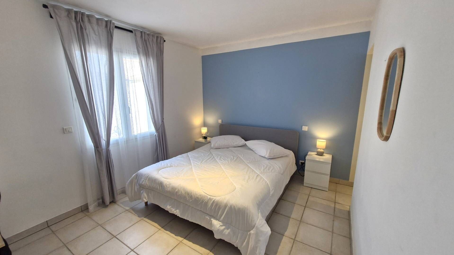 Een slaapkamer met een bed, twee nachtkastjes met lampen, een raam met gordijnen en een blauwe wand.