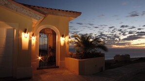 A building with a large arched entrance, a palm tree, and a sunset view. - MONTECRISTO Charming 3-bedroom villa with AC in marvelous Cabo San Lucas (Cabo San Lucas)
