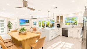 A modern kitchen with white cabinets, a wooden dining table, and a built-in dishwasher. - Luxe Pool Retreat:  Heated Pool, Game Room, Sleeps 14 (Fort Lauderdale)