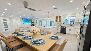 A modern kitchen with white cabinets, a dining area with a wooden table set for six, and a ceiling fan. - Luxe Pool Retreat:  Heated Pool, Game Room, Sleeps 14 (Fort Lauderdale)