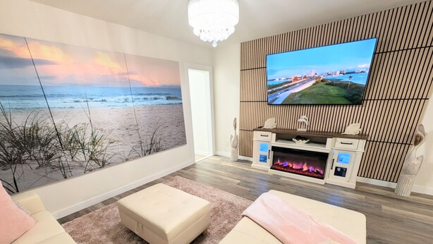 A modern living room with a large TV, a fireplace, and a view of the beach. - Fort Myers Coastal Retreat Hot Tub Yard Games (Fort Myers)