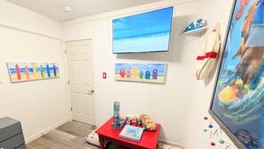 A room with a TV, colorful artwork, a red table with toys, and a blue mat. - Fort Myers Coastal Retreat Hot Tub Yard Games (Fort Myers)