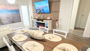 A dining room with a wooden table, white chairs, and a TV mounted on the wall. - Fort Myers Coastal Retreat Hot Tub Yard Games (Fort Myers)
