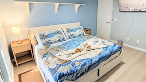 A bedroom with a bed, a nightstand, a wall-mounted TV, and a ceiling fan. - Retro Coastal Fort Myers Retreat Spa Fire Pit (Fort Myers)