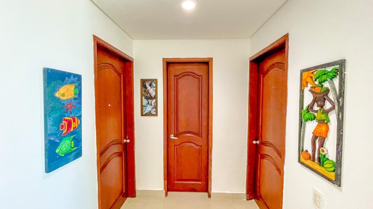 Un pasillo con dos puertas de madera y una puerta central, flanqueado por obras de arte coloridas.