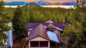 A house with a sloped roof, surrounded by dense forest and mountains in the background.