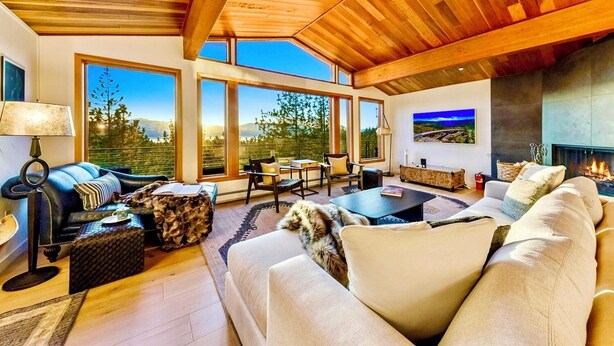 A spacious living room with a high ceiling, large windows, a fireplace, and a view of the outdoors.