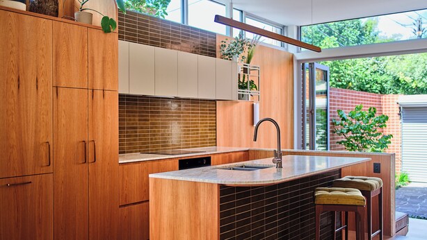 Une cuisine moderne avec des meubles en bois, un grand îlot central doté de tabourets et une vue sur l’extérieur.