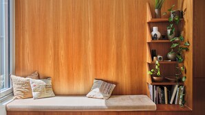 Un banc en bois avec des coussins, une bibliothèque avec des plantes et des livres.