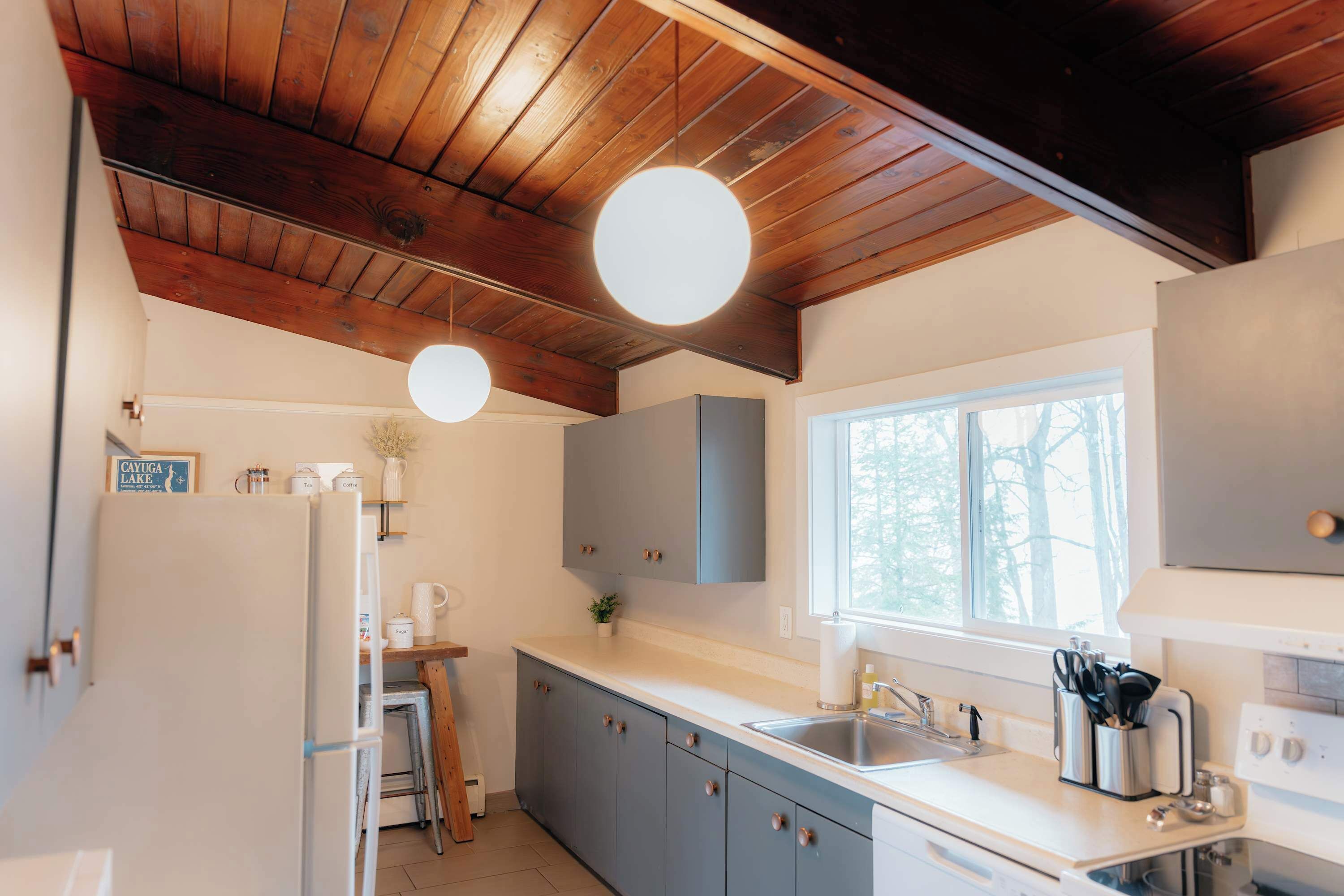 A modern kitchen with wooden ceiling beams, a large window, and a sink.