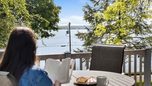 Une personne est assise à une table, devant un livre, et peut admirer un lac et une terrasse en bois.
