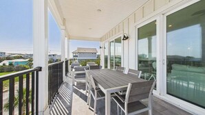 Ett takförsett utomhusområde med ett bord och stolar, stora fönster och utsikt över det omgivande bostadsområdet.