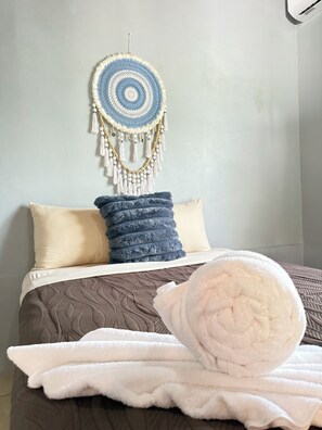 A neatly made bed with a brown quilt, two pillows, and a macrame wall hanging. - Cozy 2-bedroom house in delightful La Fortuna with AC (La fortuna)