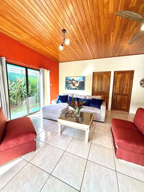 A living room with a glass coffee table, red sofas, a grey sofa, and a wooden ceiling. - Cozy 2-bedroom house in delightful La Fortuna with AC (La fortuna)