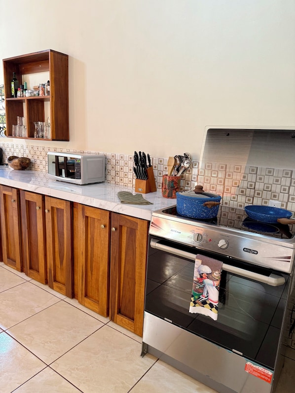 A kitchen with wooden cabinets, a microwave, a stove, and a tiled backsplash. - Cozy 2-bedroom house in delightful La Fortuna with AC (La fortuna)