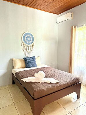 A neatly made bed with a brown bedspread and a decorative wall hanging. - Cozy 2-bedroom house in delightful La Fortuna with AC (La fortuna)